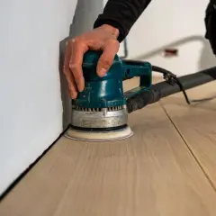 Mano che usa una levigatrice per levigare il parquet, rendendolo liscio e pronto per la finitura.
