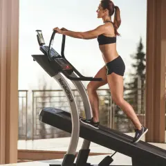 Kobieta w sportowym stroju wykonuje intensywne bieganie na bieżni, ciesząc się treningiem na świeżym powietrzu.