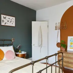 A cozy bedroom with a dark green accent wall, white door, and a terracotta arch. This space shows how to make a small bedroom look bigger with light bedding and strategic decor.
