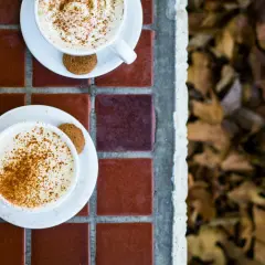 Två koppar med krämig pumpkin spice latte, toppade med kanel och en pepparkaka. Perfekt för ett mysigt pumpkin spice latte recept.