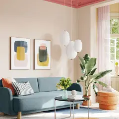 Ein Wohnzimmer mit blauem Sofa, Kunstwerken und einem orangefarbenen Hocker. Die Decke ist in einem kräftigen Pink gestrichen, was einen schönen Kontrast zur hellen Wandfarbe bildet.