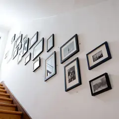 Galeria zdjęć na białej ścianie klatki schodowej, pokazująca, jak wieszać obrazy, tworząc spójną kompozycję.
