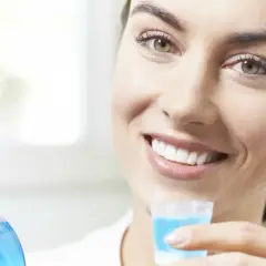 Donna sorridente tiene in mano un misurino con collutorio con clorexidina, pronto per l'uso.