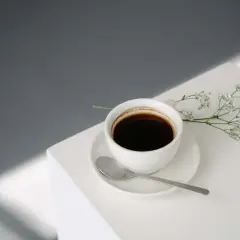 En vit kaffekopp med en sked och en liten blomsterkvist. Kanske inte det bästa valet om man är dålig i magen av kaffe på morgonen.