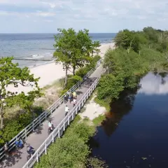Ścieżka rowerowa wzdłuż plaży i jeziora. Ludzie cieszą się piękną pogodą, korzystając z rozwiniętej infrastruktury rowerowej.