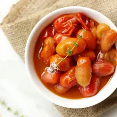 Deliciosos tomates cherry confitados en un cuenco blanco, adornados con tomillo fresco y una flor morada.