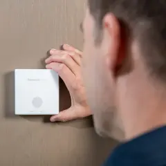 Mężczyzna sprawdza, czy czujnik czadu ma datę ważności. Urządzenie Honeywell Home zamontowane na ścianie.