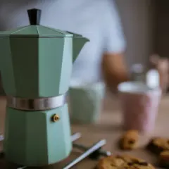 Moka verde pronta per il caffè, ma forse manca qualcosa per capire perche la moka non fa il caffe. Biscotti e tazze sullo sfondo.