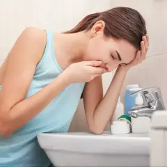 Kobieta w łazience, z ręką na ustach, doświadcza mdłości w ciąży.