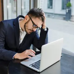 Zestresowany mężczyzna w garniturze pracuje przy laptopie, próbując skrócenie pauzy do 7 godzin.