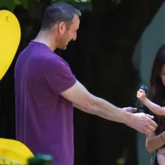 Mężczyzna w fioletowej koszulce podaje rękę kobiecie trzymającej dziecko na placu zabaw.