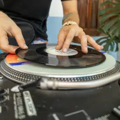 DJ kładzie winylową płytę na gramofonie. Kolorowy **cover** pod nią dodaje klimatu.