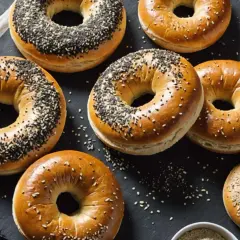 Plusieurs bagels dorés, certains parsemés de graines de sésame noires et blanches, prêts pour la cuisson.