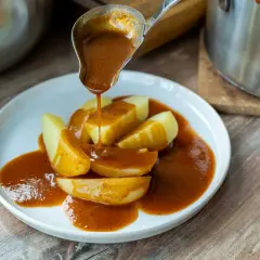 Eine Schöpfkelle gießt eine köstliche braune Sauce über Kartoffelspalten auf einem Teller.