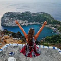 Widok na zatokę Anthony Quinn na Rodos. Kobieta z rękami w górze podziwia jeden z najpiękniejszych miejsc na wyspie.