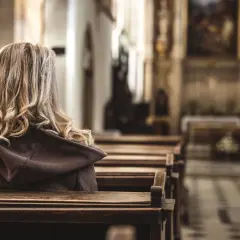 Kobieta z blond włosami siedzi w kościele, odwrócona tyłem. Obraz ilustruje badanie CBOS praktyki religijne.