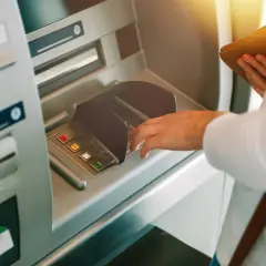 Dłoń wpisuje PIN przy bankomacie, mając nadzieję, że nie zniknęły pieniądze z konta.