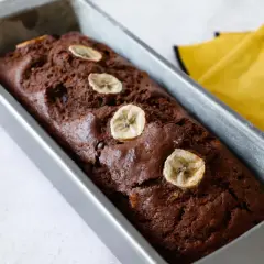 Plumcake banana e cioccolato appena sfornato, decorato con fettine di banana essiccata, in uno stampo metallico.
