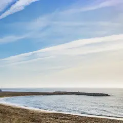 Playa de Macenas en Almería, con un muelle y el sol brillando en el mar.