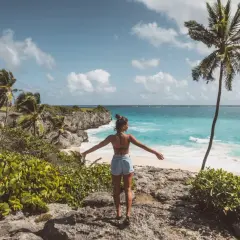 Kobieta z rozłożonymi rękami podziwia turkusowe morze i palmę. Idealne Barbados wakacje.