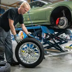 Mekaniker byter däck på en grön Audi. Det är dags för hjulskifte datum, så bilen lyfts upp på en billyft.