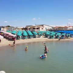 Plage de Marina di Pisa animée, avec des rangées de parasols et de chaises longues sur le sable, et des baigneurs profitant de l'eau claire sous un ciel bleu.