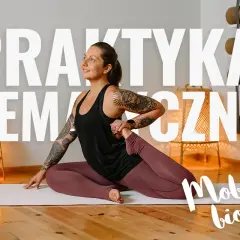 Kobieta w pozycji kapotasana, ćwicząca mobilność bioder. W tle rośliny i maty do jogi.