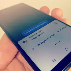 Smartfon z Asystentem Google, który czeka na **wyszukiwanie głosowe**. Widoczne opcje: "Poznaj więcej funkcji Asystenta", "Cześć, w czym mogę pomóc?", "Zagrajmy w coś".