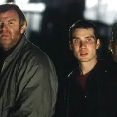Trzech ocalałych, w tym mężczyzna z groźną miną, przemierzają mroczne ulice w świecie po apokalipsie. To scena z filmu "28 dni później".