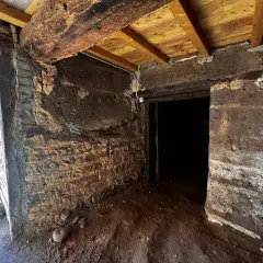 Intérieur d'une maison en pisé en ruine, murs érodés, poutres apparentes. Danger de délabrement.