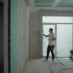 Pracownik nakłada gładź agregatem. Zastanawiasz się, ile kosztuje położenie gładzi? Sprawdź!