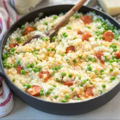 Pyszne risotto z kiełbasą i groszkiem, podane w czarnej patelni, z drewnianą łyżką.