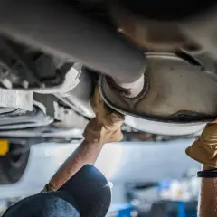 Mani guantate lavorano sul sistema di scarico, forse sostituendo il catalizzatore auto.