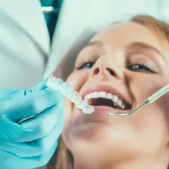 Dentysta w niebieskich rękawiczkach pokazuje pacjentce przezroczystą szynoprotezę.