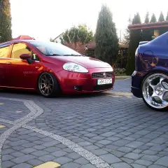 Czerwony Fiat Grande Punto 1.4 z przyciemnianymi szybami i sportowymi felgami, obok niebieski samochód. Rozmiar opon dopasowany do modyfikacji.