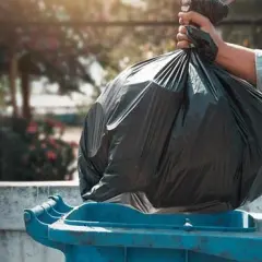 Mano depositando bolsa de basura en contenedor azul. ¿Quién paga la tasa de basura en un alquiler?
