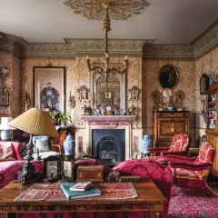 A lavish Victorian interior design with ornate wallpaper, plush red furniture, a fireplace, and antique decor.
