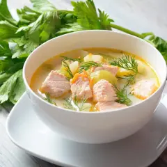 Aromatyczna zupa rybna przepis: kremowy bulion z łososiem, ziemniakami i koperkiem, obok świeża natka pietruszki.