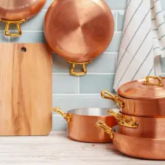 Utensilios de cobre apilados y colgados, junto a una tabla de cortar. Aprende como limpiar cobre para que brillen así.