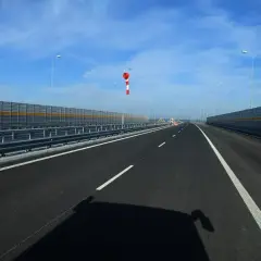 Pusta droga dwujezdniowa z barierami dźwiękochłonnymi po bokach. W oddali widać wiatrowskaz.