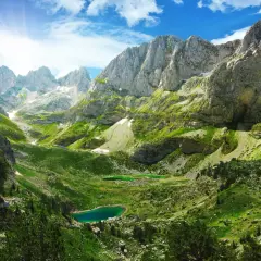 Magnifique paysage de montagne pour un trek en Albanie, avec des lacs d'un bleu profond et des pentes verdoyantes sous un ciel ensoleillé.