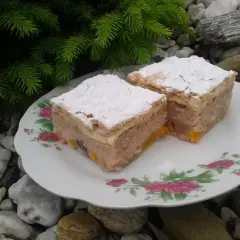 Dwa kawałki ciasta z kisielem na oleju, posypane cukrem pudrem, na talerzyku z różami, wśród kamieni i gałązek choinki.