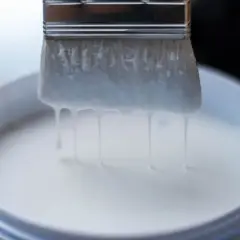 Pennello intriso di vernici all'acqua, gocciolanti in un secchio bianco.