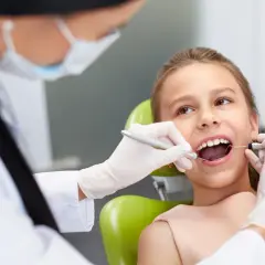 Dziecko u dentysty, które czeka na znieczulenie. Stomatolog w rękawiczkach bada ząb dziewczynki.