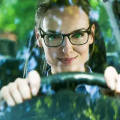 Frau mit Brille am Steuer, bereit zum Autofahren.