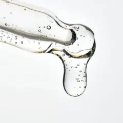 Kropla przejrzystego serum z pęcherzykami powietrza, zawierającego kwasy LHA, spływa z pipety.