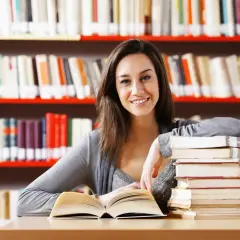 Uśmiechnięta studentka z książkami w bibliotece.