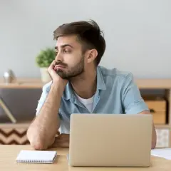 Homme ennuyé devant son ordinateur, illustrant la sédentarité. Il s'ennuie, signe de sédentarité.