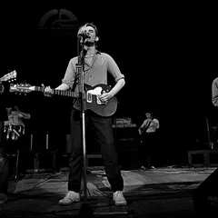 Zespół grający punk rock na scenie. Wokalista z gitarą, gitarzysta po lewej, saksofonista po prawej.