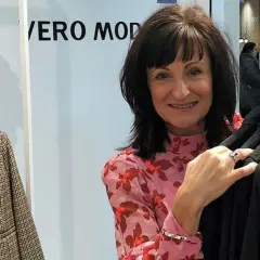 En glad kvinna i en blommig blus vid en klädställning med kläder från en Vero Moda återförsäljare.